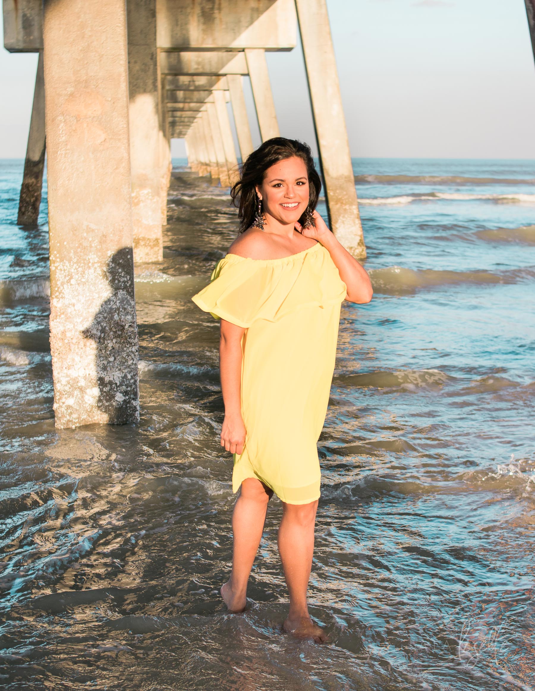 brunette woman standing under pier wearing yellow sundress