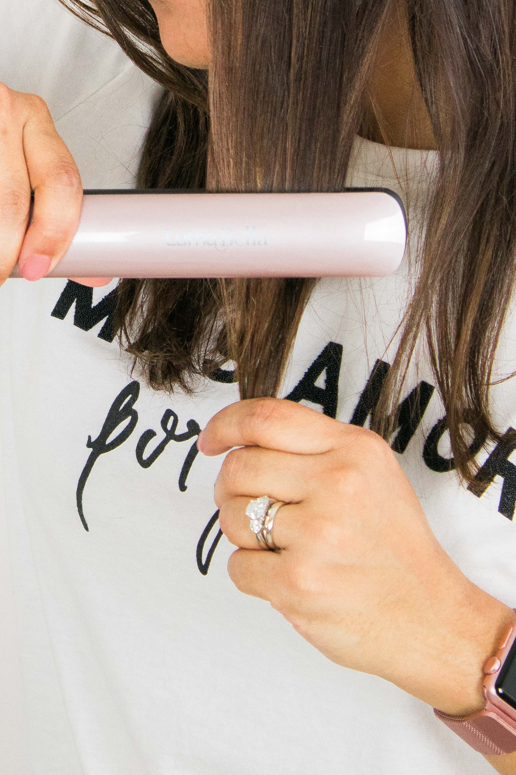 Woman flat ironing her hair, wearing t-shirt that reads "Mas Amor por favor"