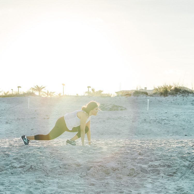 woman in sprint position at beach with solar flare behind her