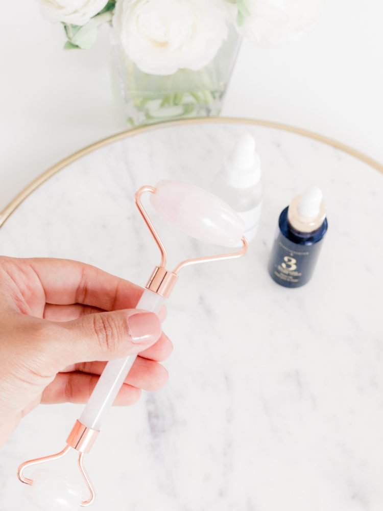 Hand holding rose quartz jade roller with Beautycounter Balancing Oil in the background